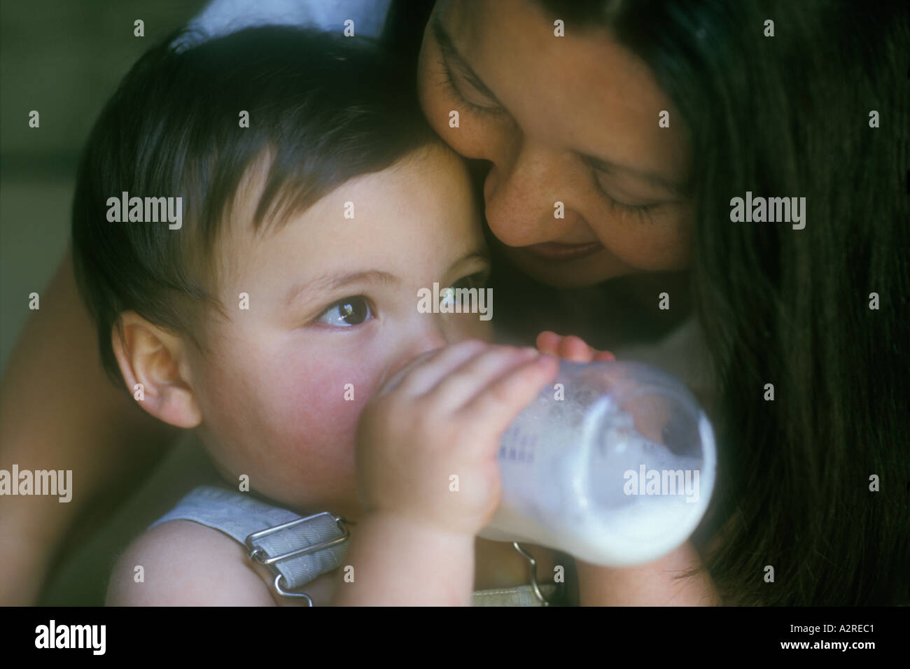 Mixed Asian Caucasian mother hugging mixed Asian Caucasian bottle feeding infant son Stock Photo