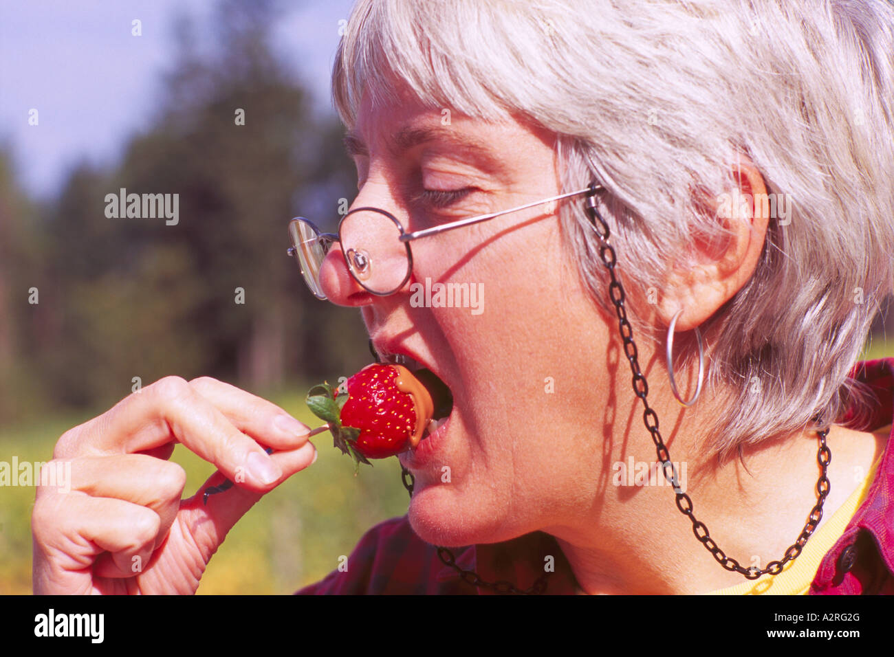 Mature Grey Haired / Gray Haired Woman wearing Glasses eating a Chocolate  Dipped Strawberry Stock Photo - Alamy