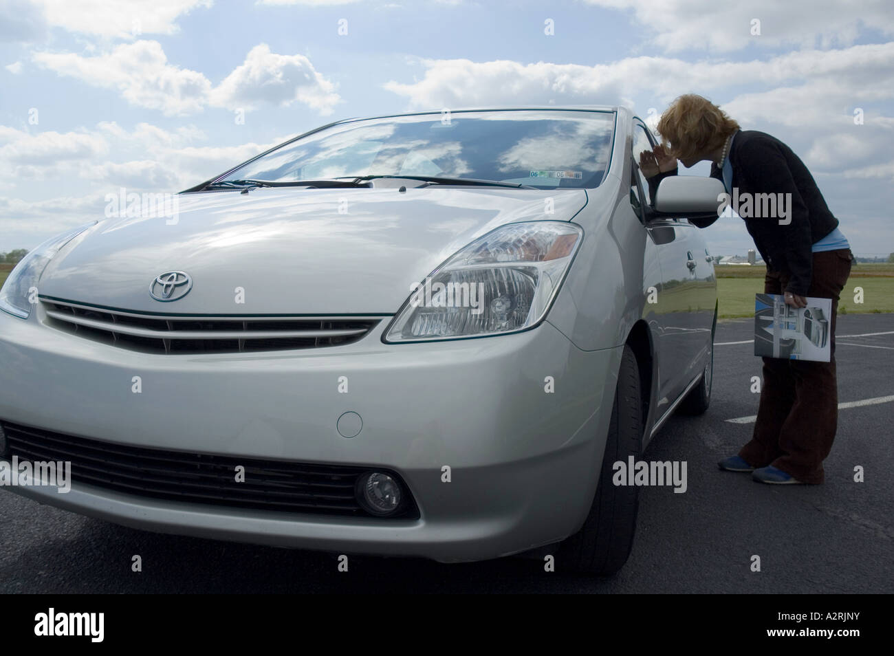 YOUNG WOMAN LOOKING AT 2004 TOYOTA PRIUS GASOLINE-ELECTRIC HYBRID CAR Stock Photo