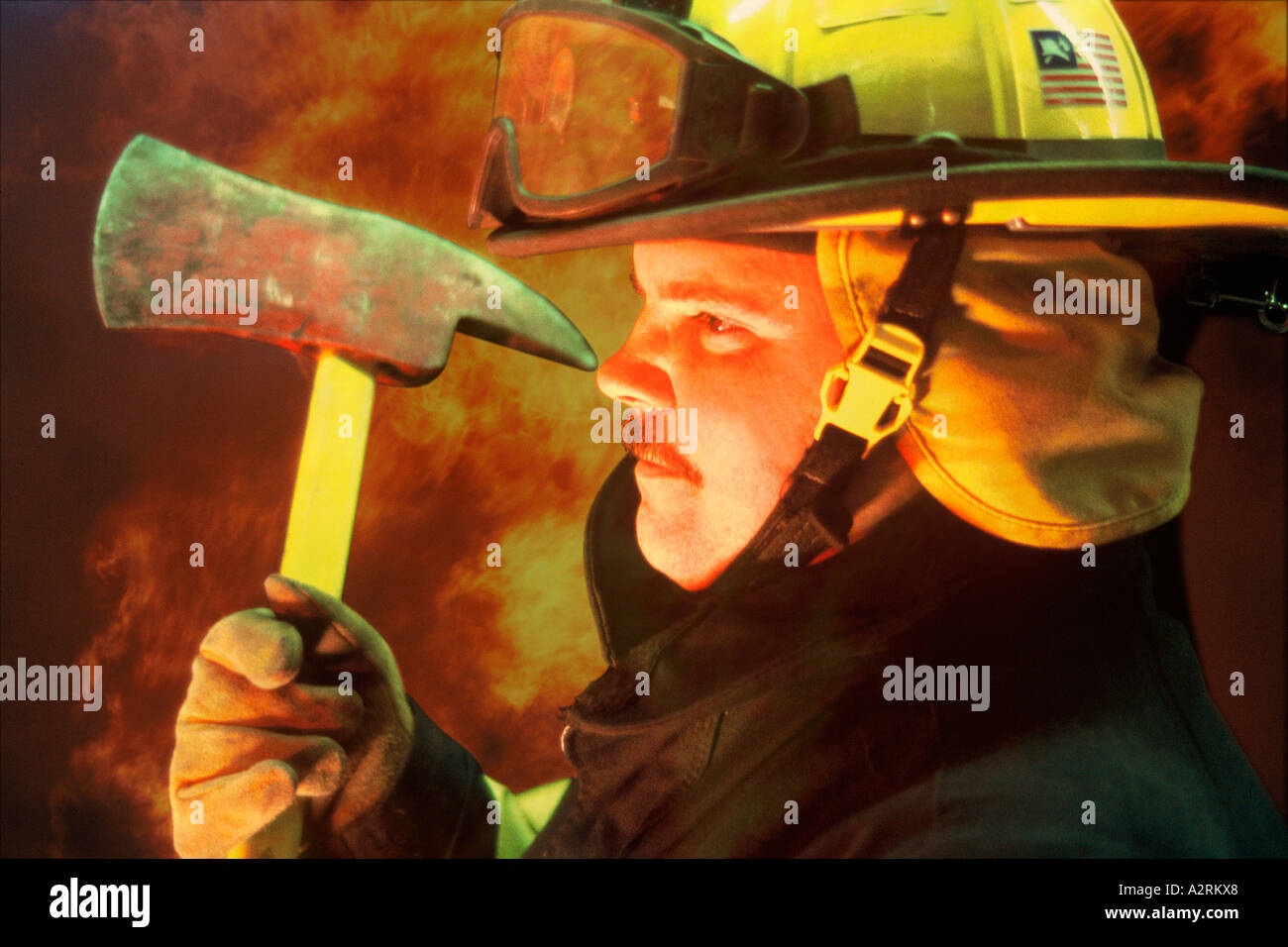 A fire fighter with an ax with fire behind him Stock Photo