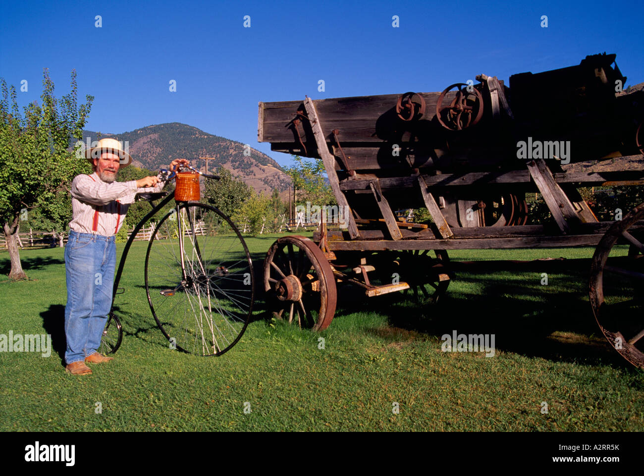 Keremeos, BC, Similkameen Valley, British Columbia, Canada - Man with Penny Farthing beside Old Wagon at Grist Mill and Gardens Stock Photo