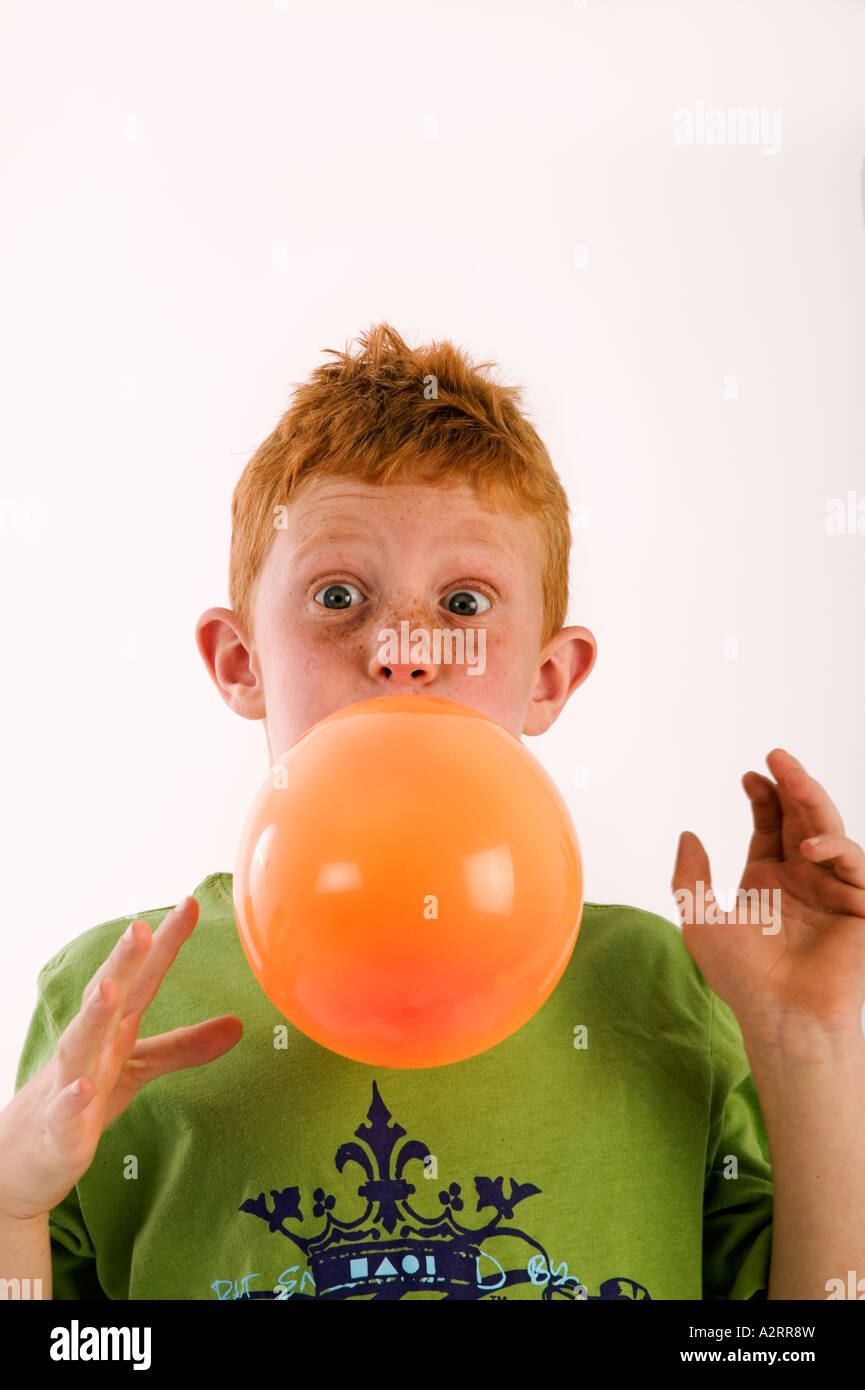 Young boy with red hair and freckles age 7 blowing up an orange balloon Model released Studio shot Stock Photo