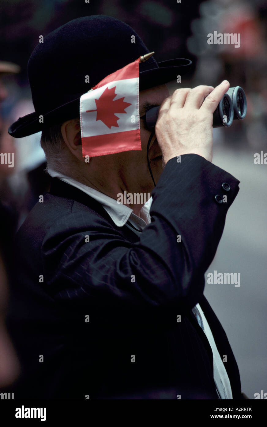 A Proud Patriotic Canadian Man celebrating Canada Day Celebration - looking through Binoculars with Flag stuck in Bowler Hat Stock Photo