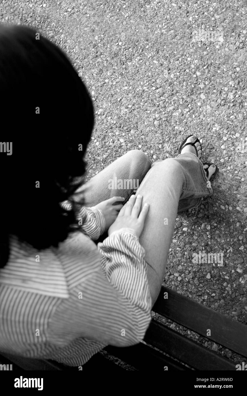 Black and white shot of young woman with blue jeans and sandals shot from above and back, sitting outdoors with hands on her lap Stock Photo