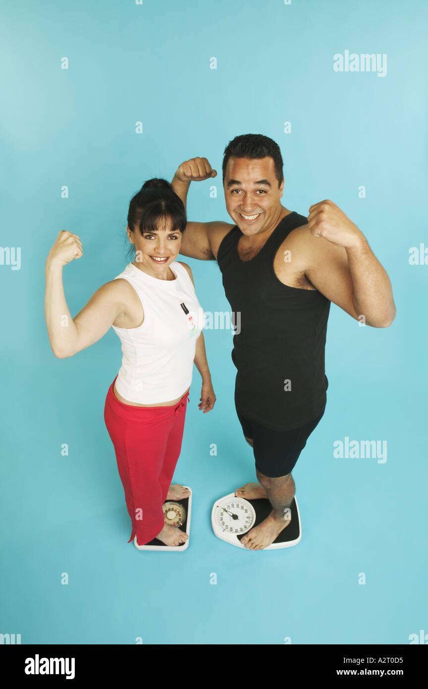 Couple standing on scales and flexing their muscles Stock Photo