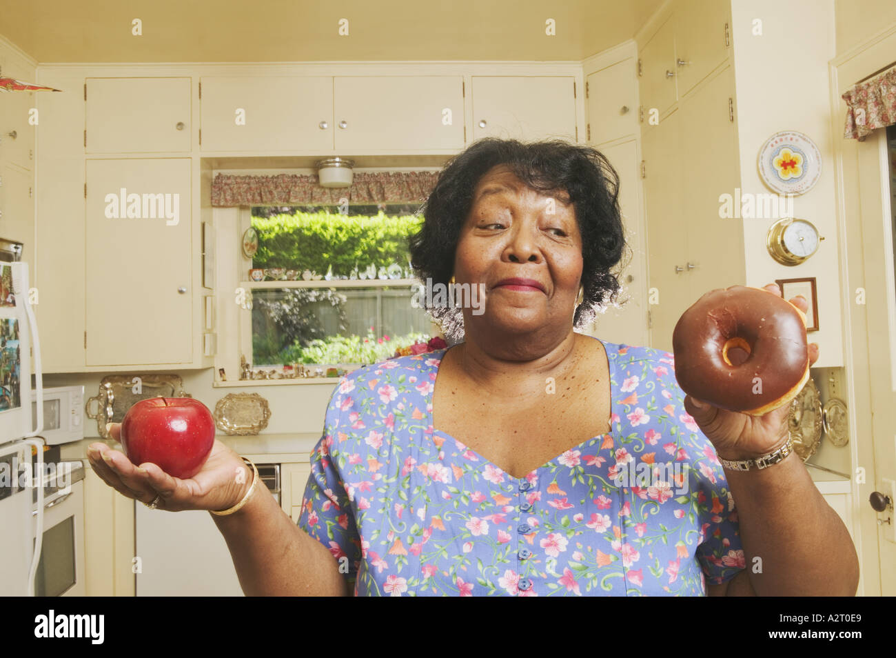 Woman deciding whether to eat an apple or doughnut Stock Photo