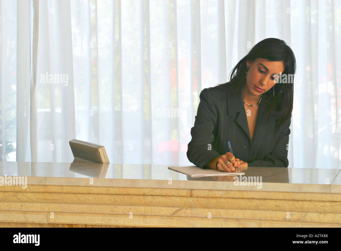 M.S of young receptionist doing some paperwork behind a hotel desk ...