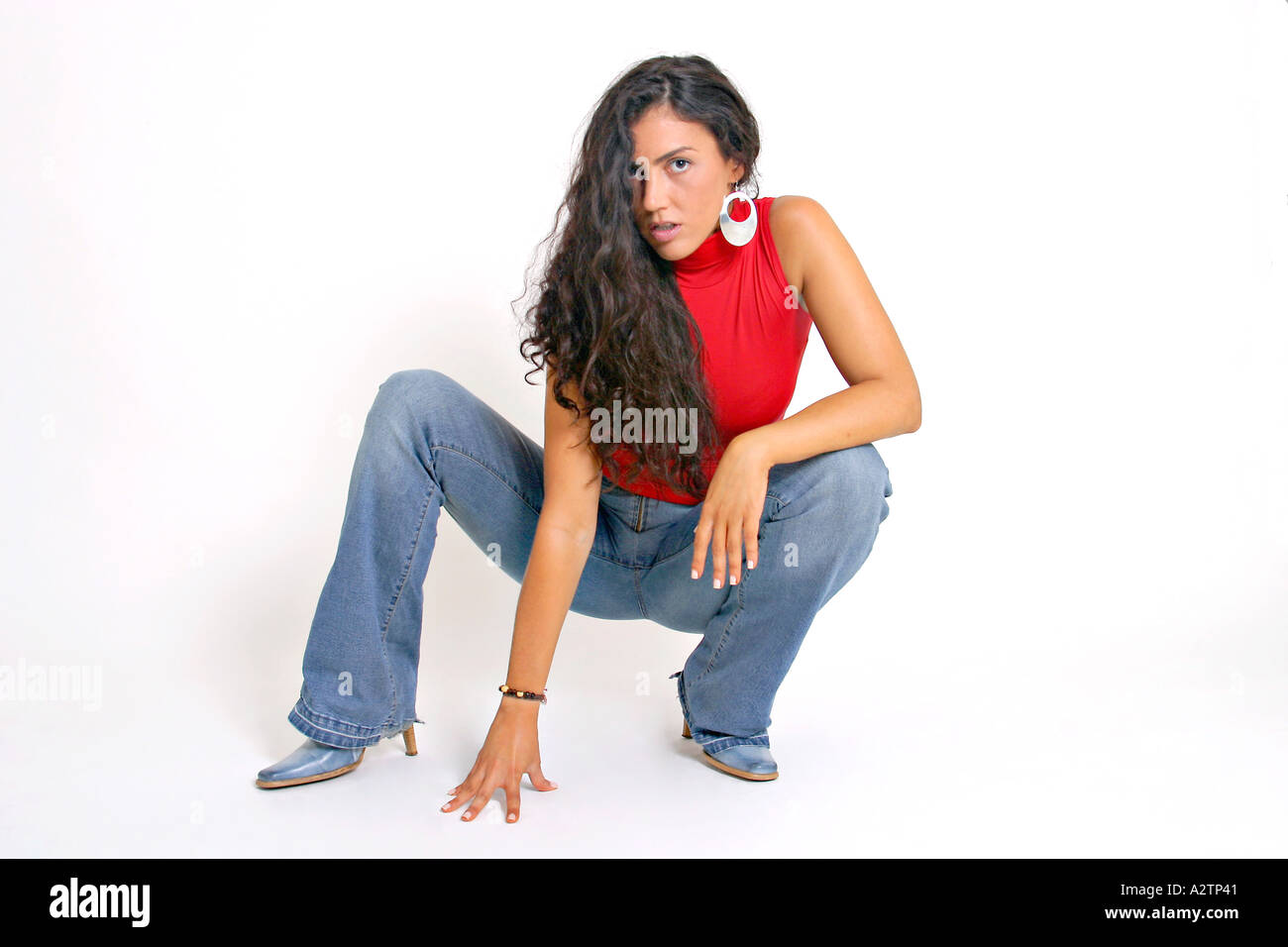 Full shot of Spanish girl with red top and jeans squatting Stock Photo