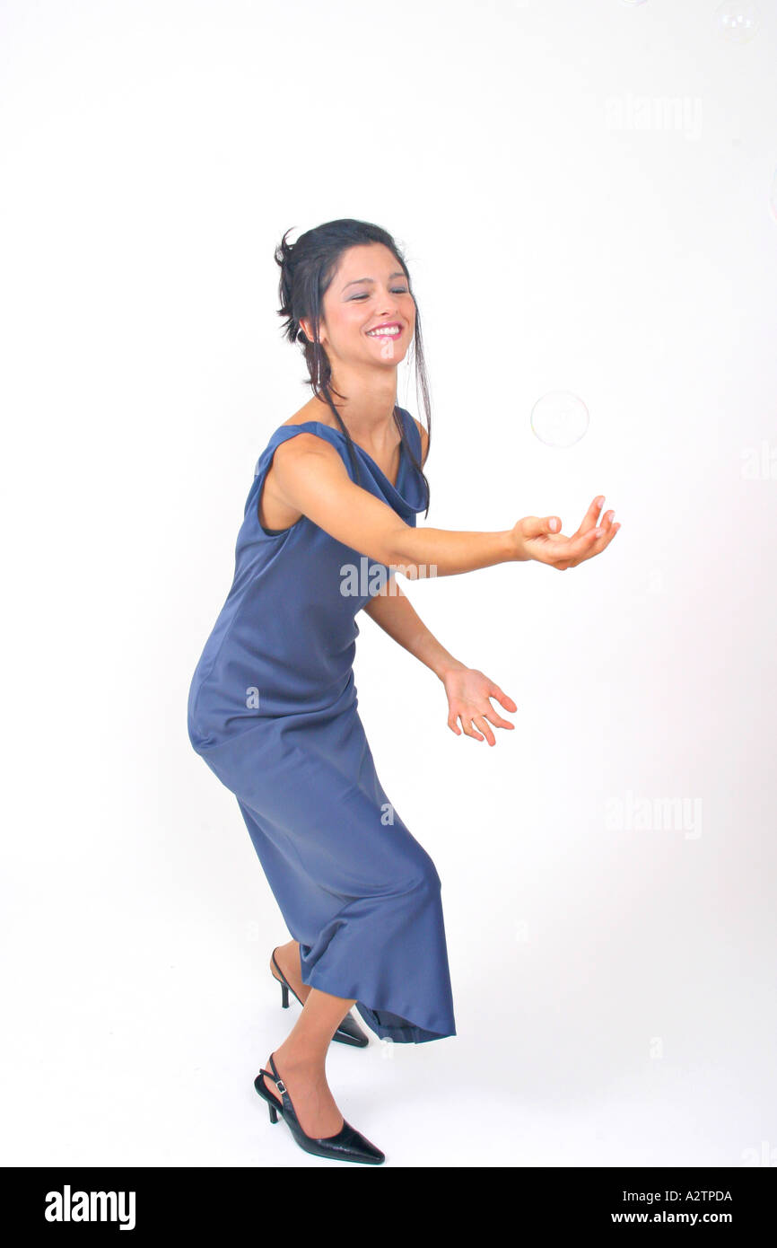 F.S. of young woman in a blue evening gown playing with soap bubbles with arm extended Stock Photo