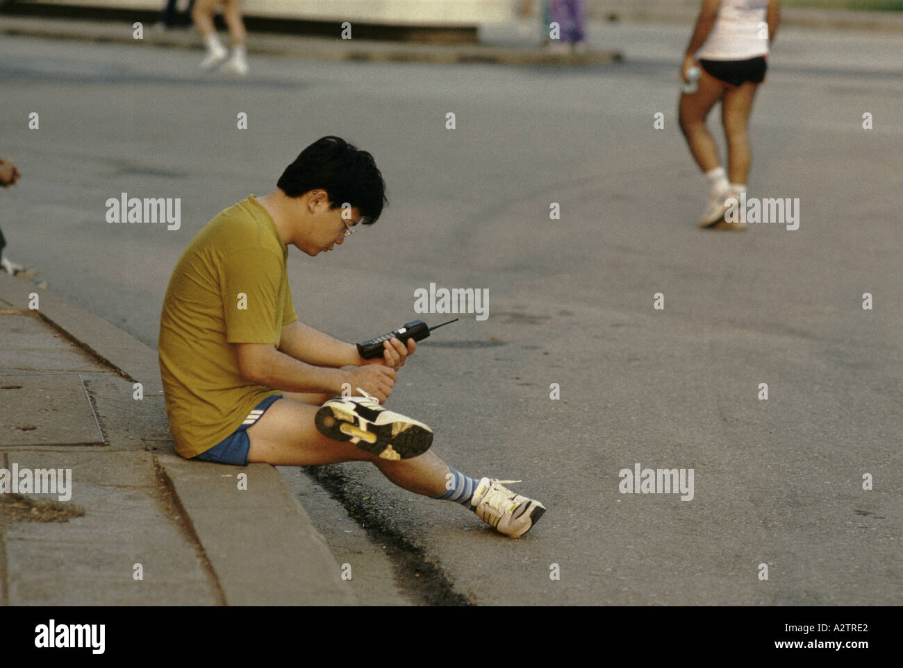 Jogger having a break sitting on the pavement in Bangkok, using his mobile phone, Thailand Stock Photo