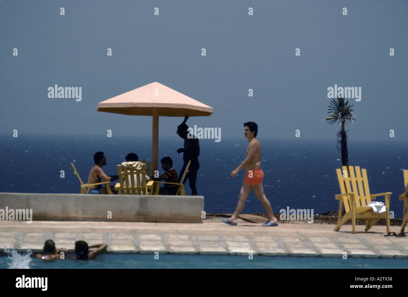 Holidaymakers stand around and swim in the pool with the blue sea behind them, Cayo Largo, Cuba Stock Photo