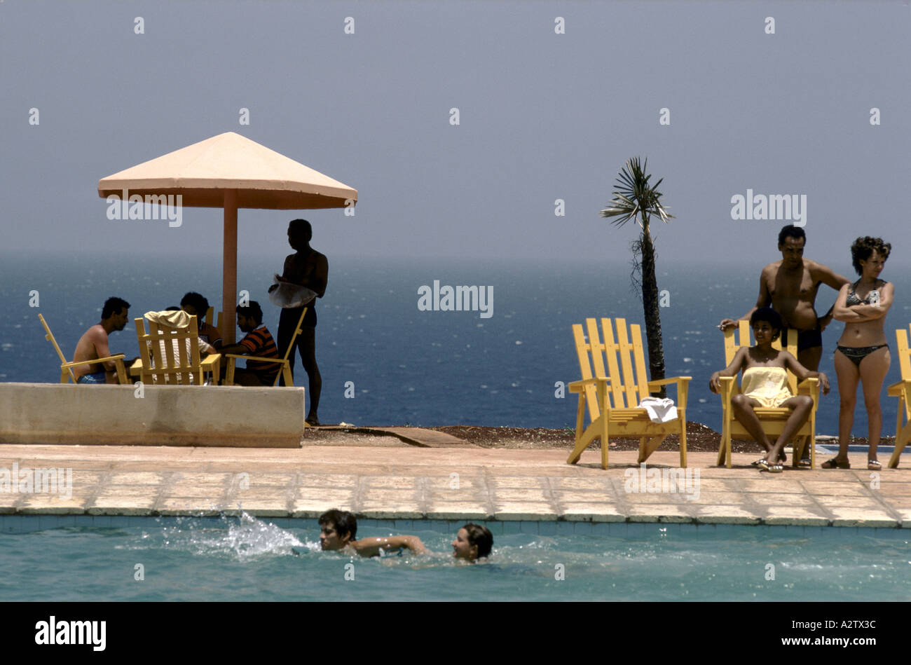 Holidaymakers stand around and swim in the pool with the blue sea behind them, Cayo Largo, Cuba Stock Photo