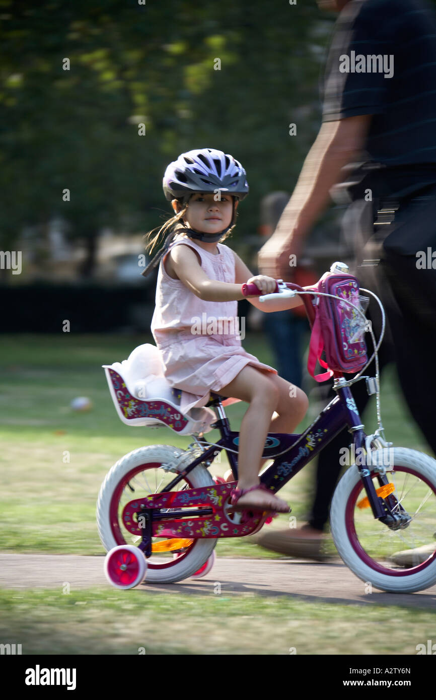 Young asian girl riding a bicycle with stabilisers in the evening in Grosvenor Square Mayfair London W1 England Stock Photo