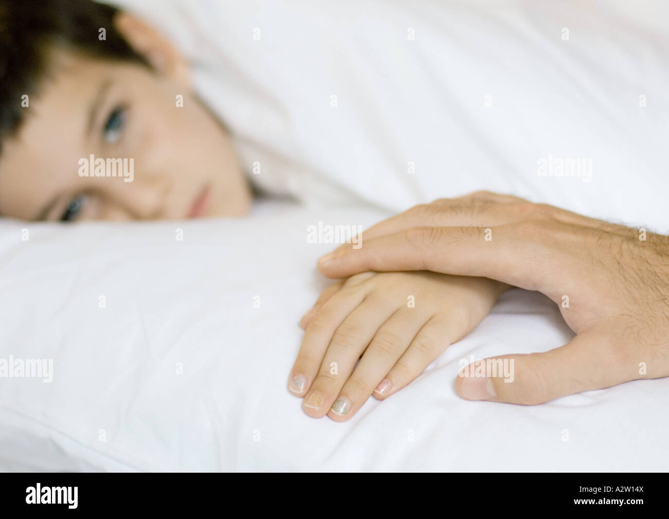 Child lying in bed, father's hand on child's Stock Photo