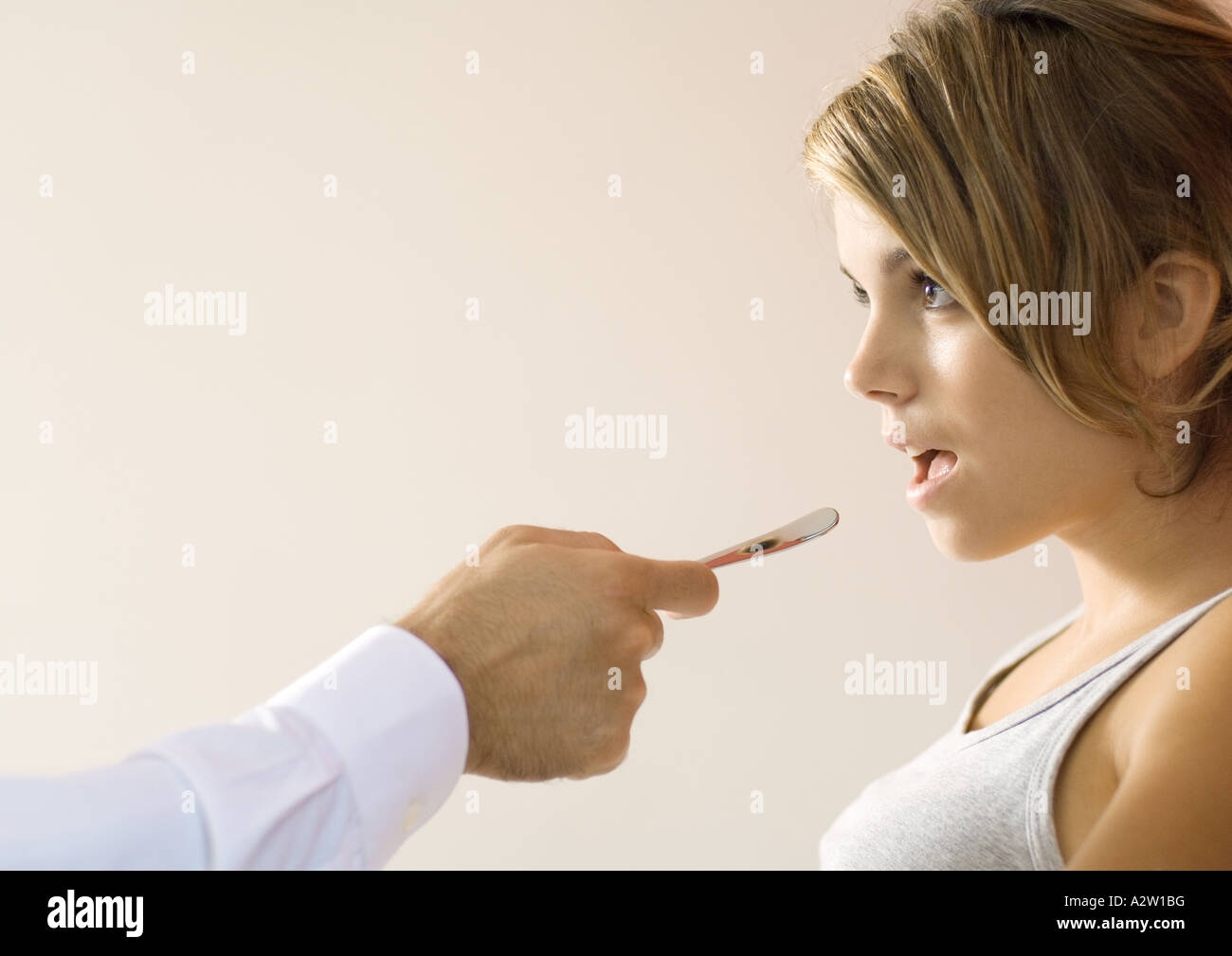 Doctor holding out tongue depressor toward young woman's mouth Stock