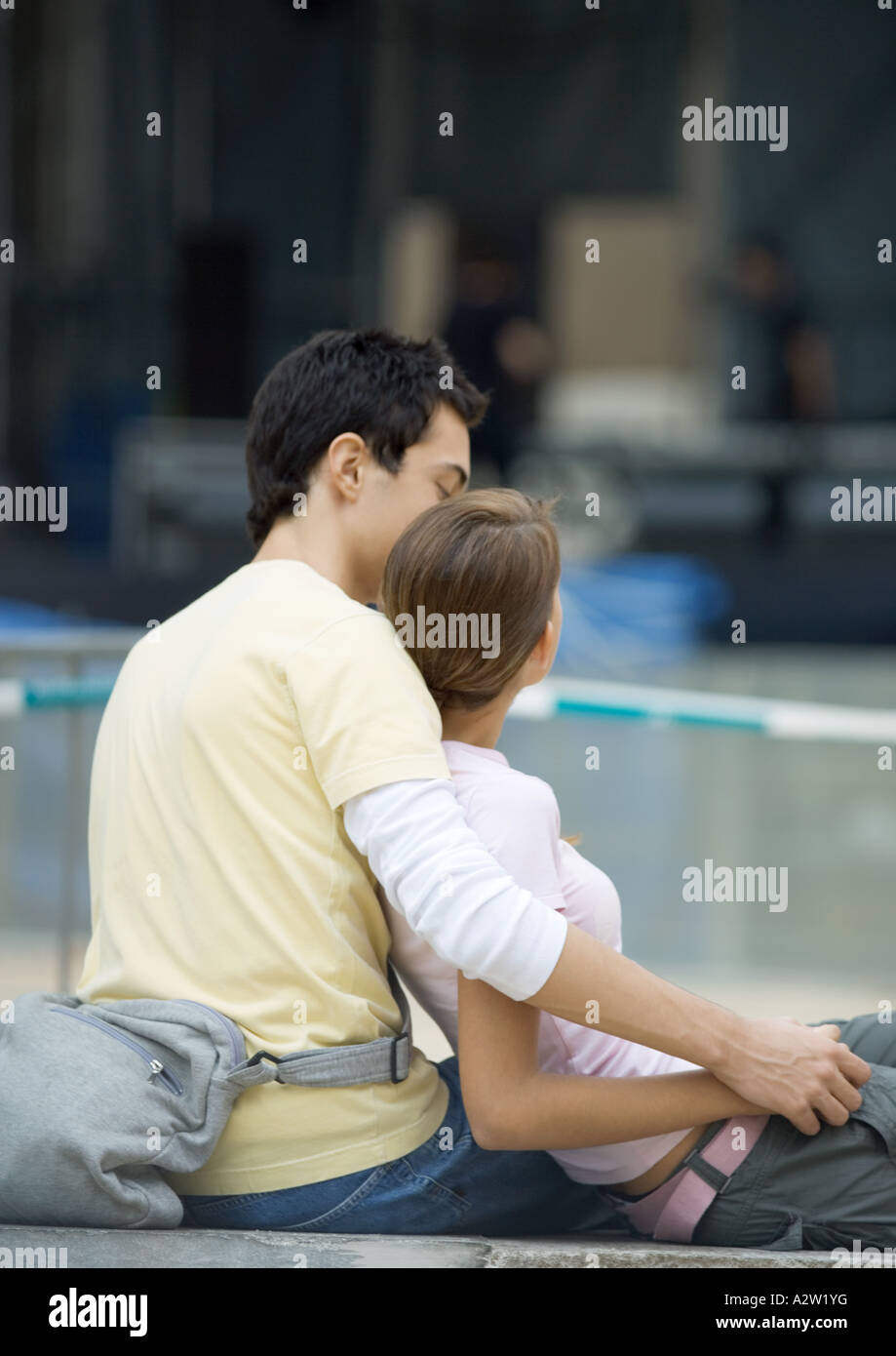 Teenage couple sitting outdoors, girl leaning against boy Stock Photo