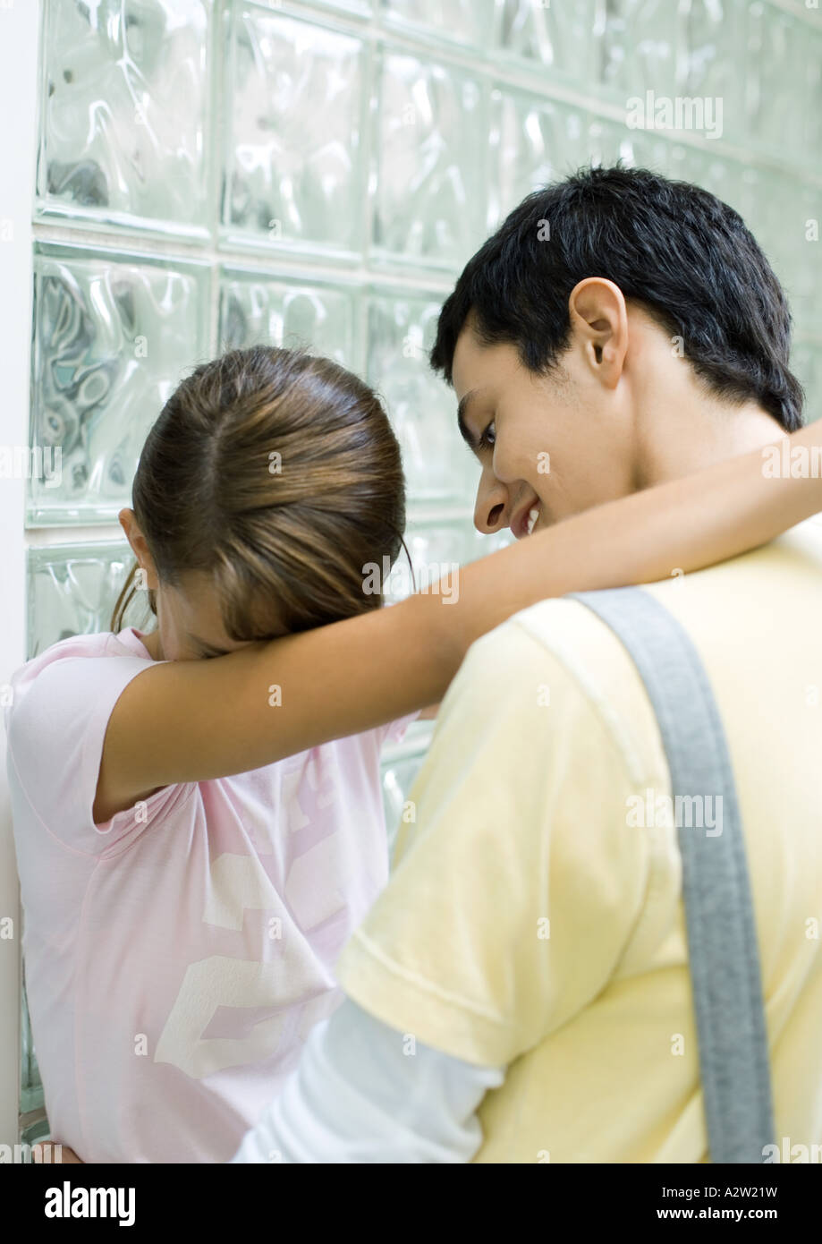 Teenage couple standing with arms around each other, girl hiding ...