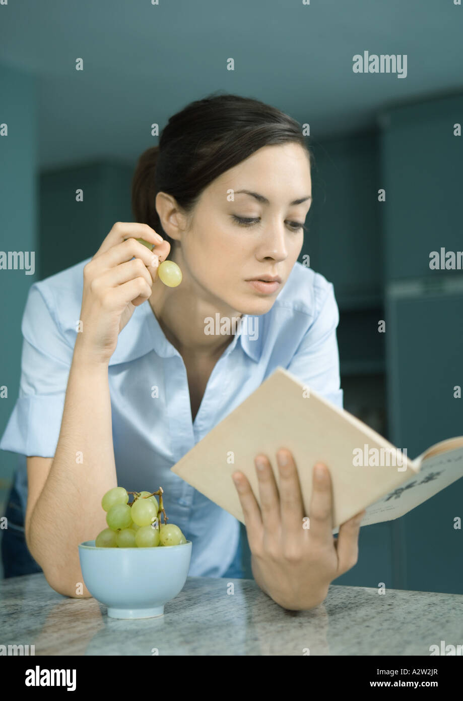Woman reading book and eating grapes Stock Photo Alamy