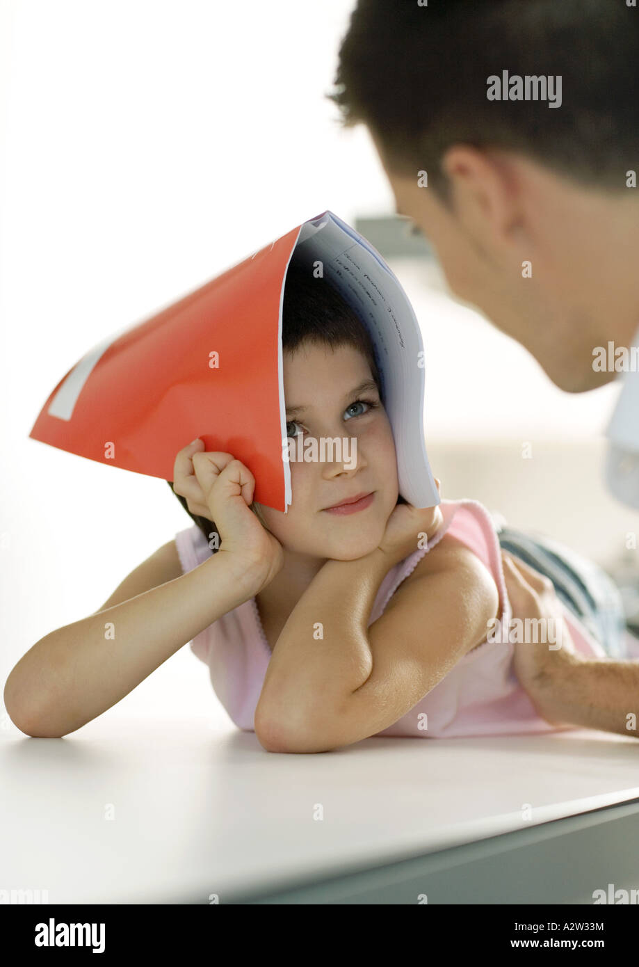 Child holding notebook over head, looking at father Stock Photo