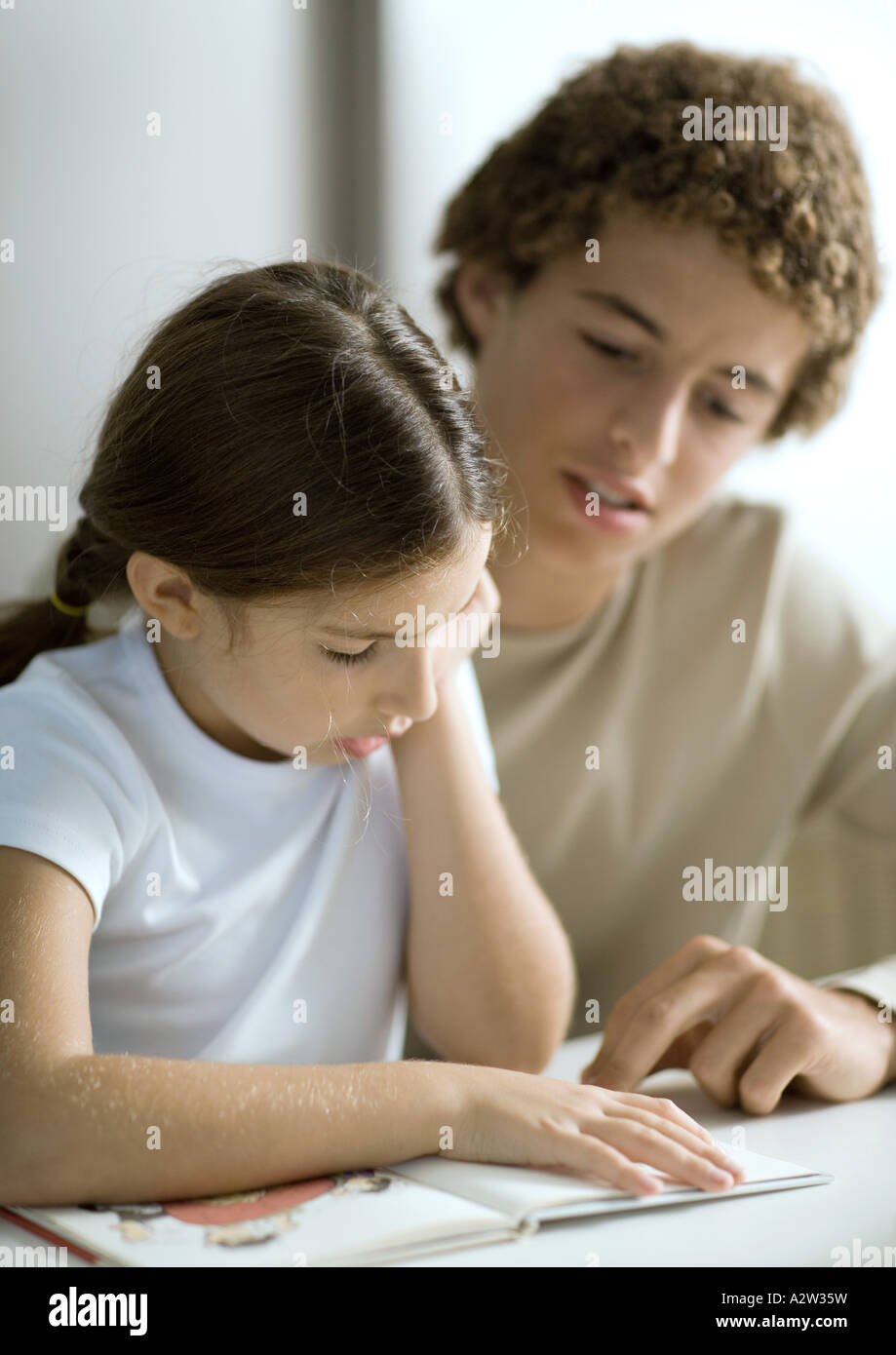 Adolescent boy listening to little sister read Stock Photo