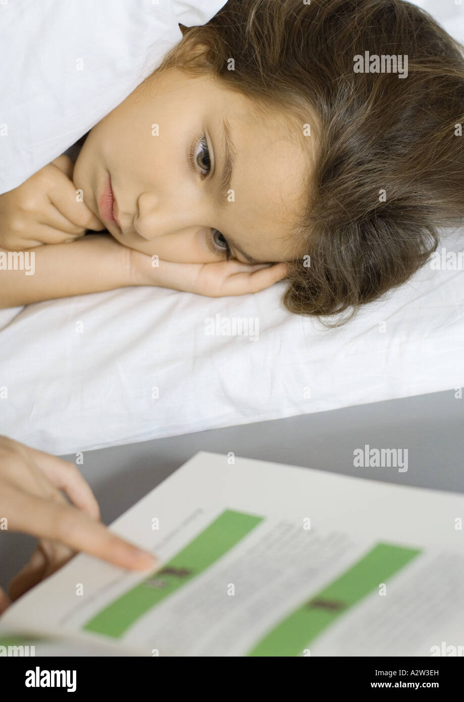 Girl lying in bed, listening to mother read from book Stock Photo