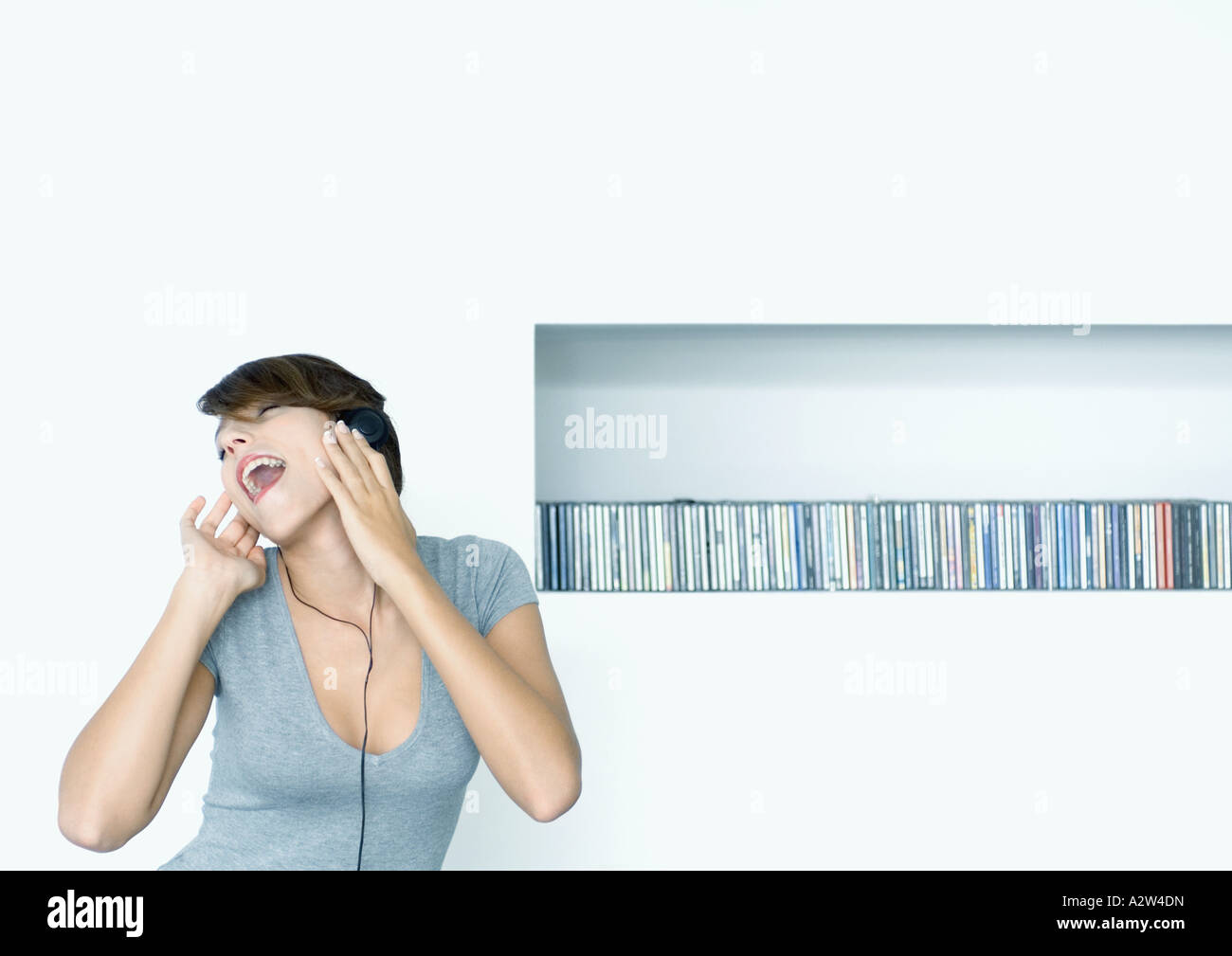 Woman listening to headphones, shelf of cds in background Stock Photo