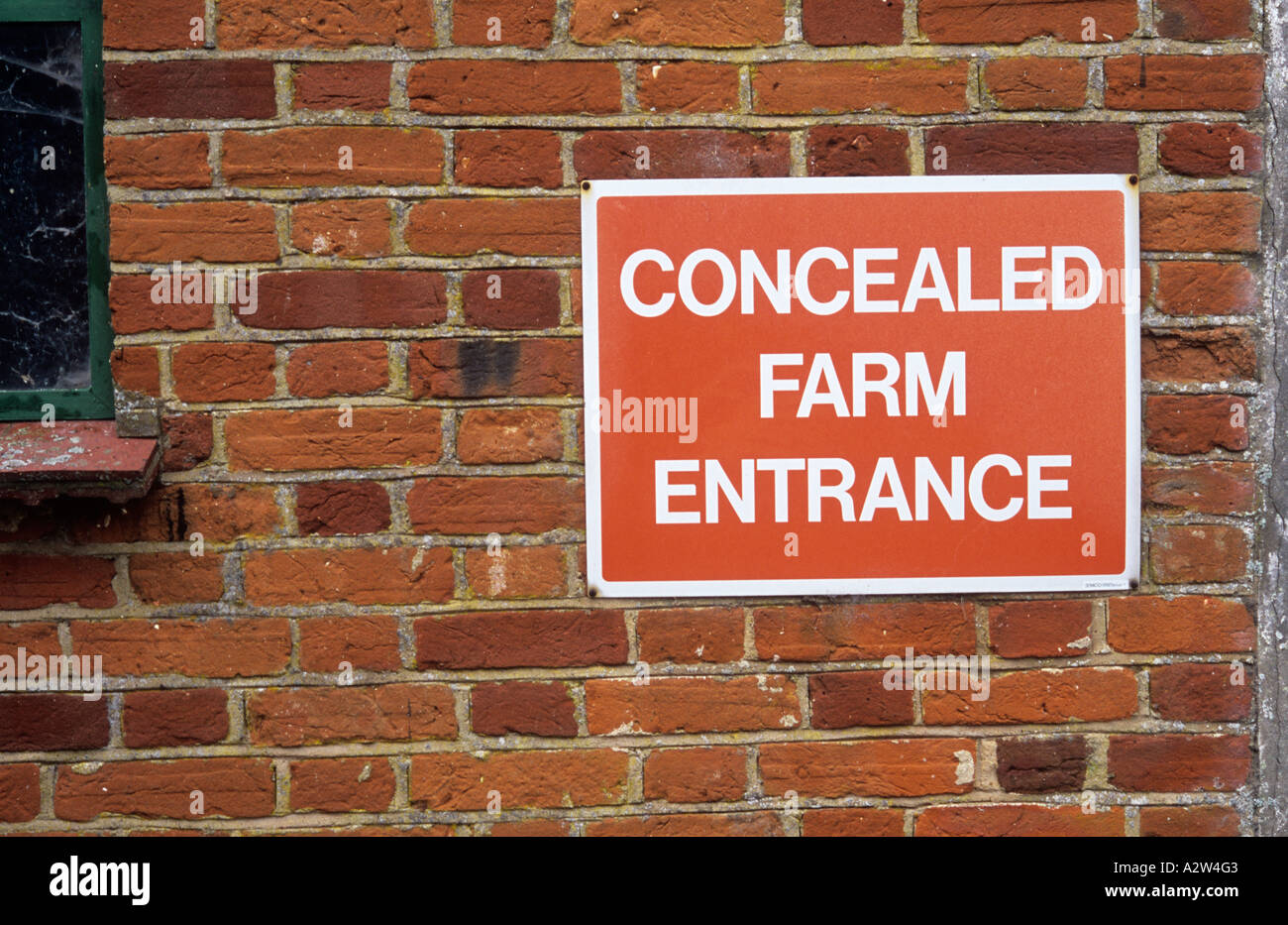 Red and white sign fixed to an orange brick wall warning of a Concealed farm entrance Stock Photo