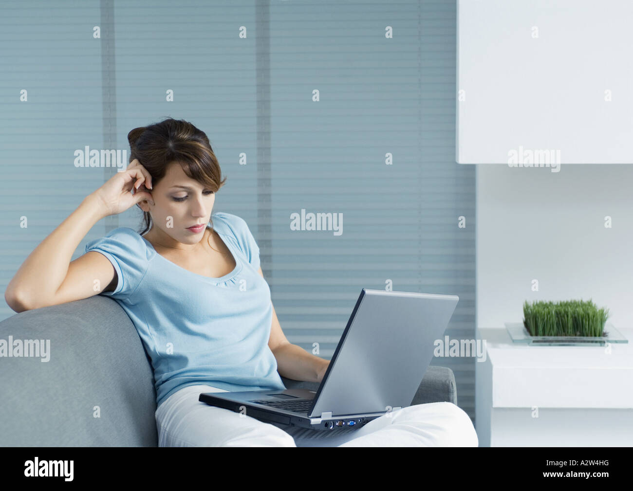 Young woman sitting on sofa, using laptop Stock Photo