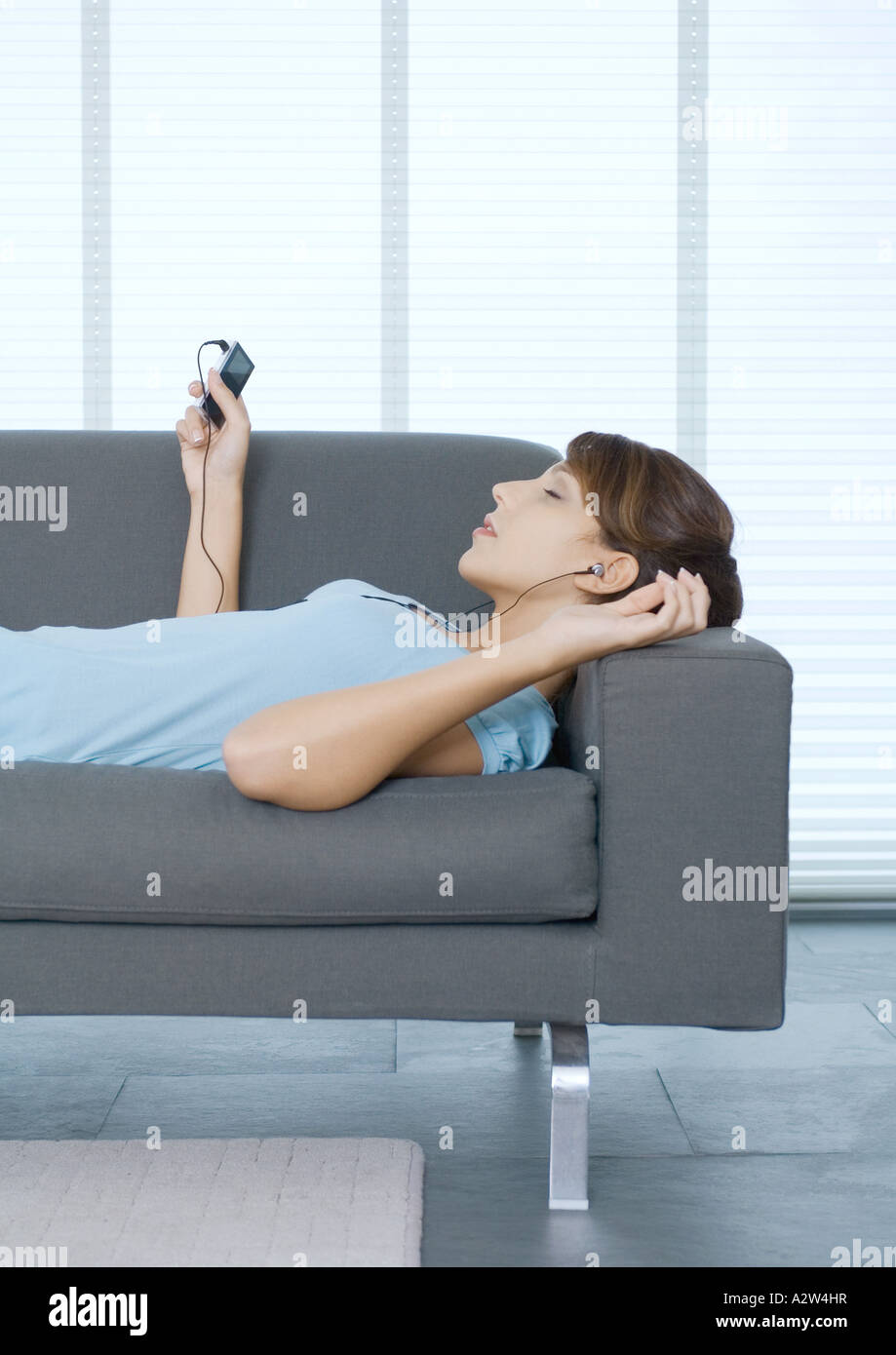 Young woman lying on sofa, listening to portable MP3 player Stock Photo