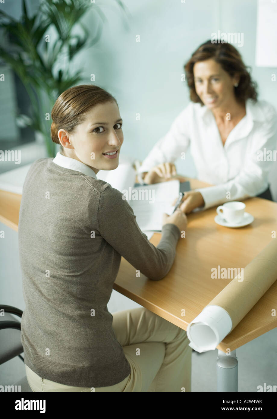 Woman sitting at table across from architect, smiling over shoulder at camera Stock Photo