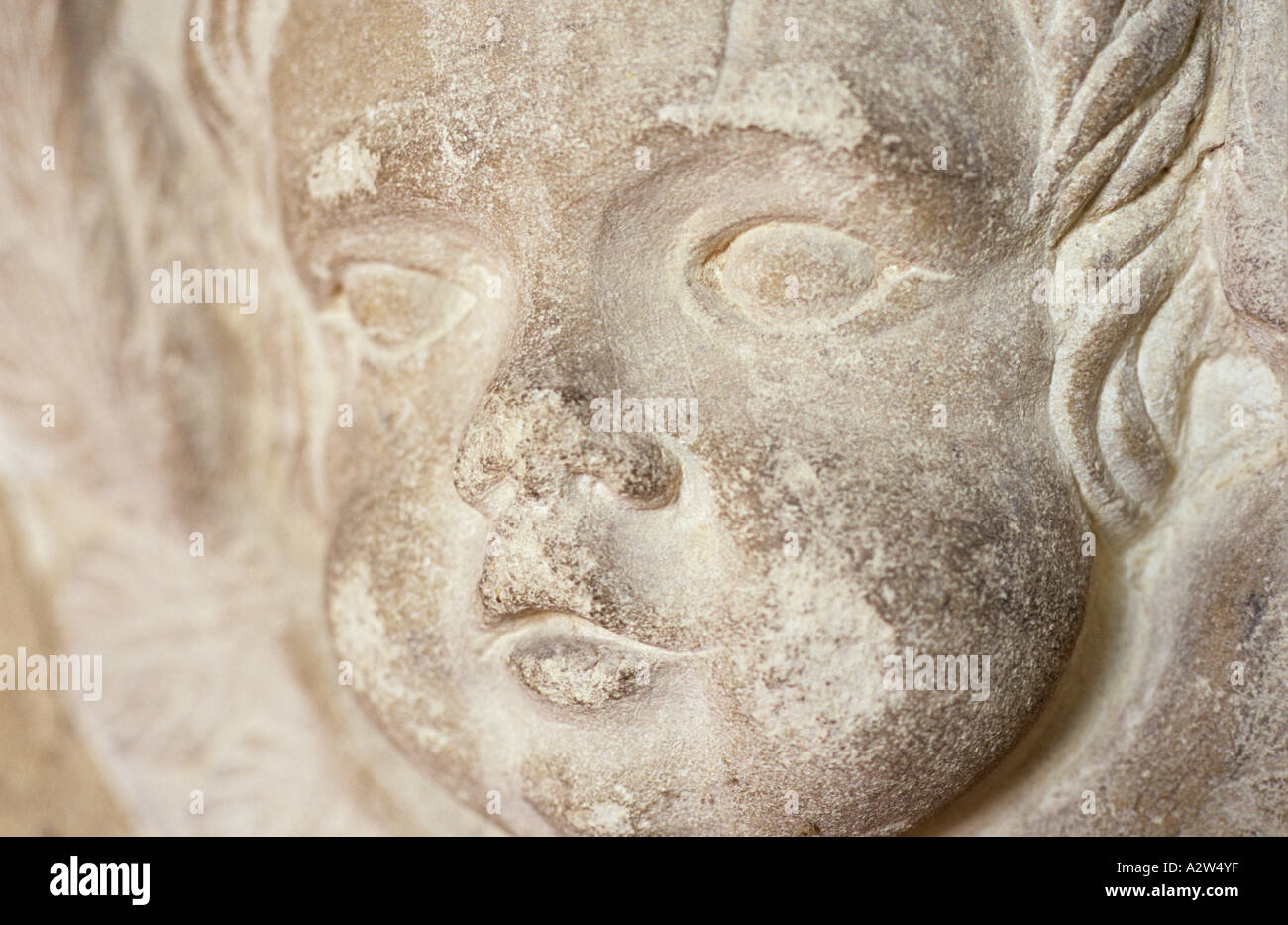 The face of a worn chipped and grubby carved stone cherub on a memorial Stock Photo