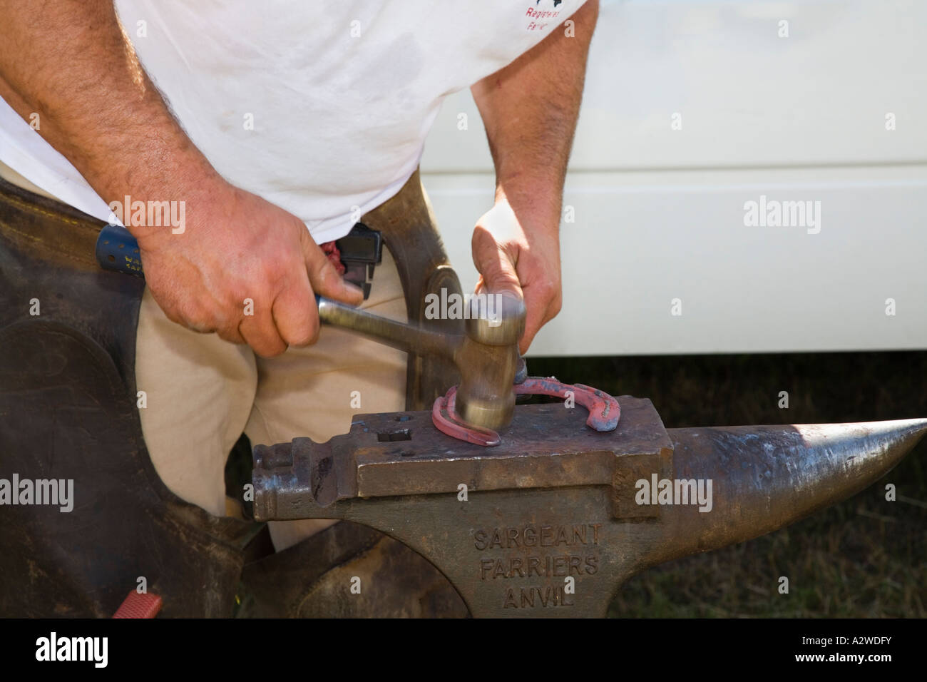 Farrier making horse shoe hammering red hot shoe on anvil Hammer