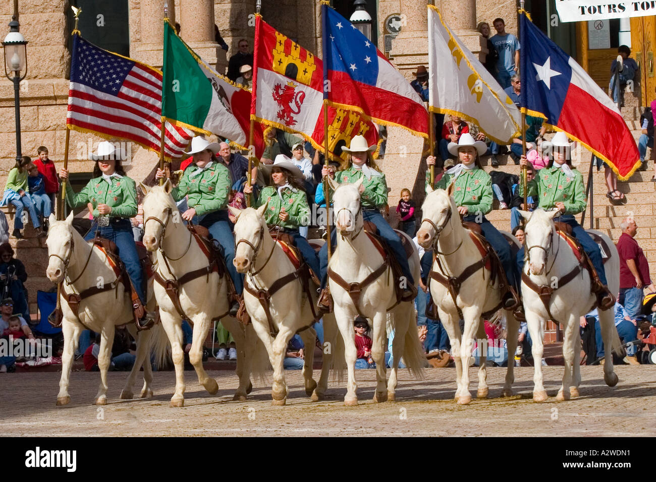 Six Cowgirls on White Horses Carry Flags That Have Flown Over Texas, America, Mexico, Spain, Confederacy, France, and Texas Stock Photo