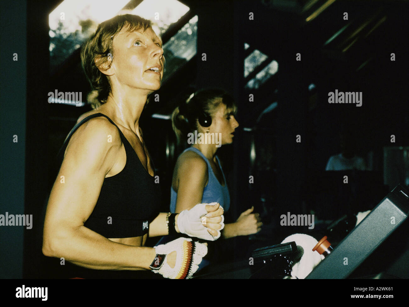 a muscular sweaty blonde woman working out docklands gym wears a black sports top and white half gloves and looks up london Stock Photo