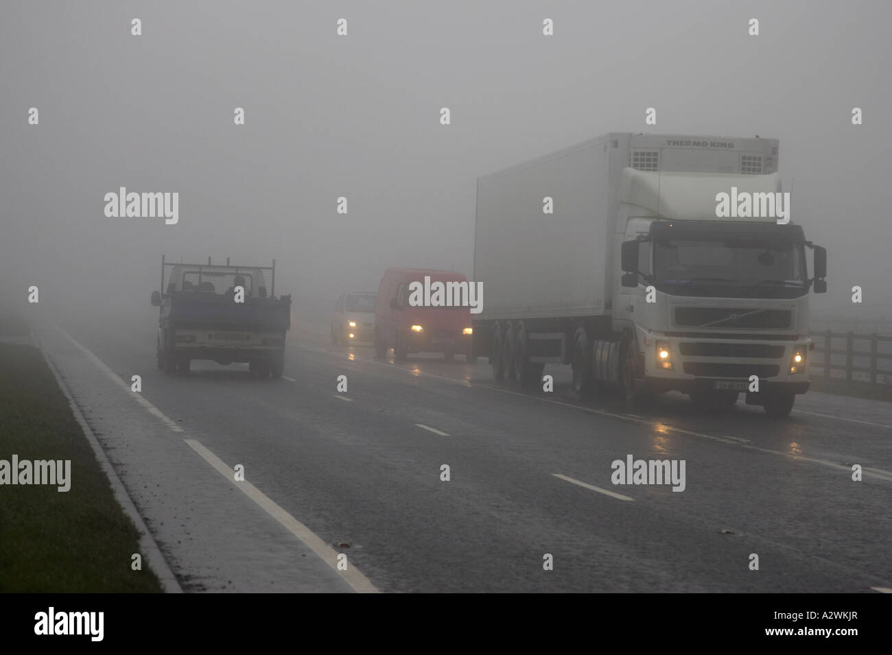 lorry and cars with dipped headlights on a main road covered in fog in northern ireland Stock Photo