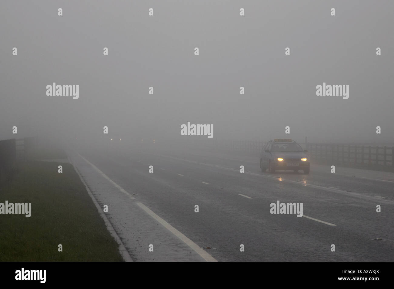 cars with dipped headlights on a main road covered in fog in northern ireland Stock Photo