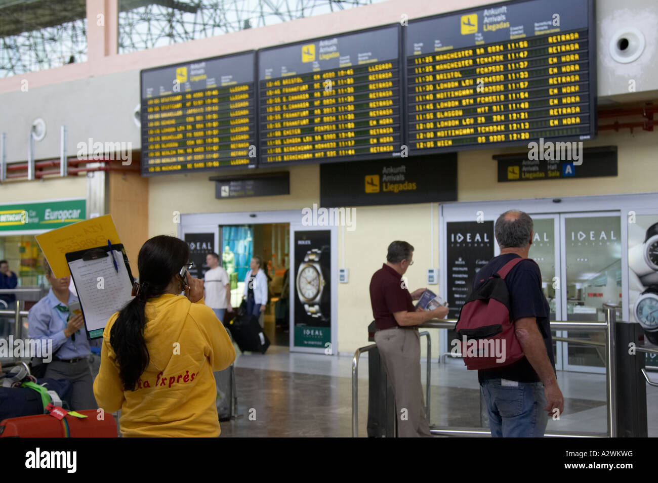 female spanish tour guide in yellow jumper waits in front of arrivals
