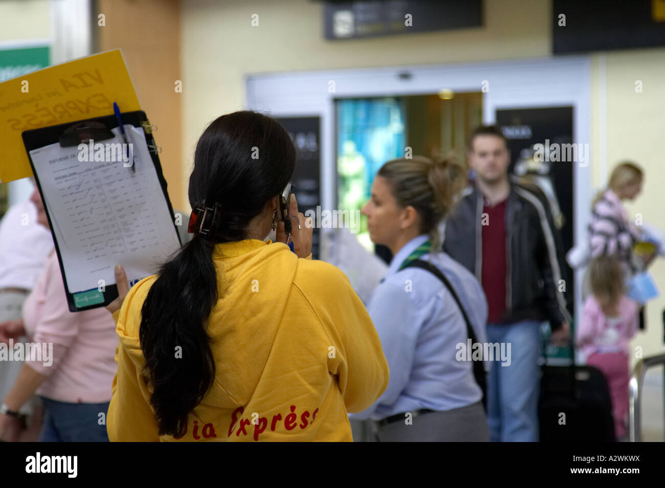 female spanish tour guide in yellow jumper on mobile phone waits in front of arrivals with list of passengers at Reina Sofia Stock Photo