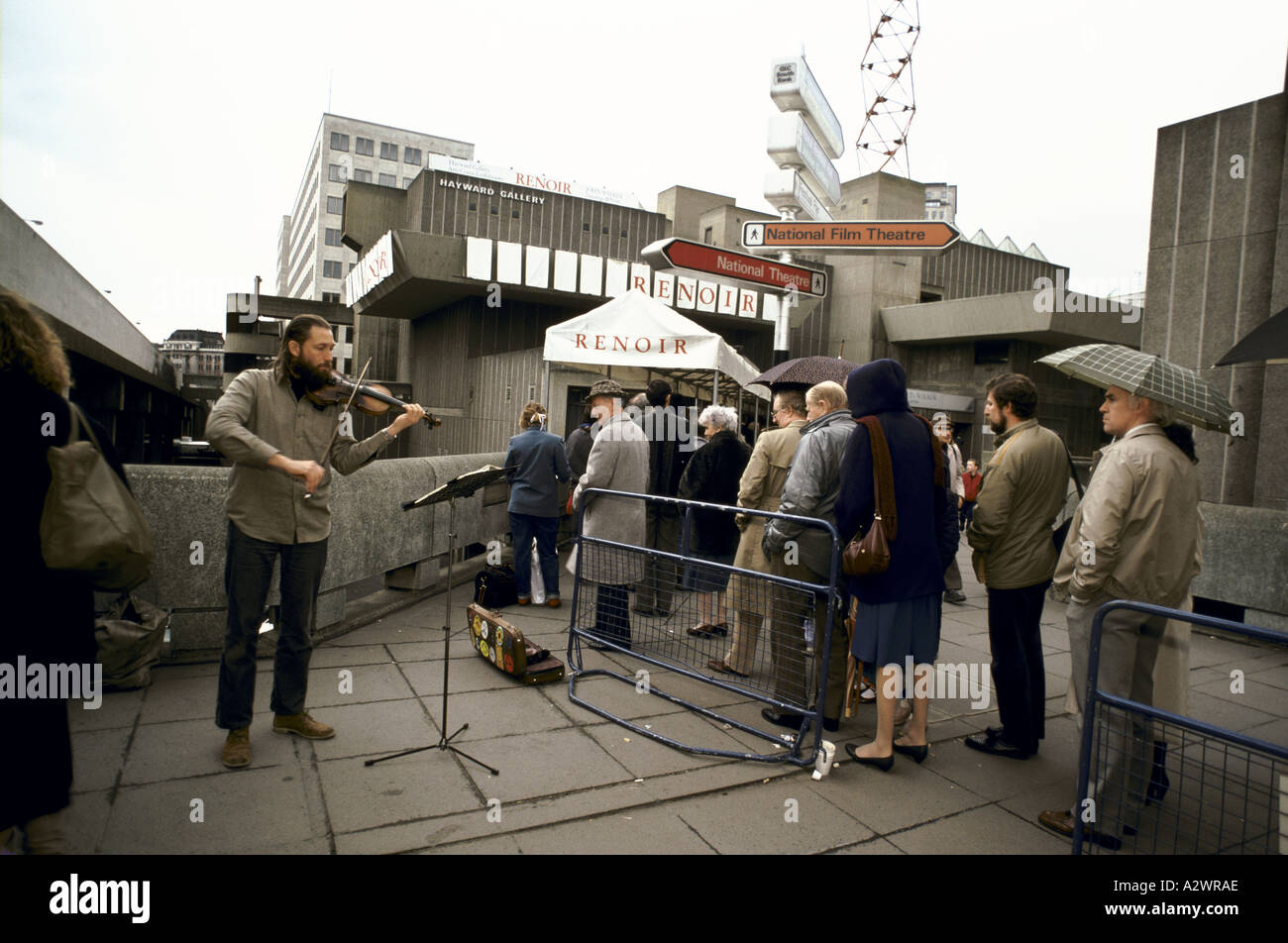 busker playing violin to people queuing to see exhibition of paintings by renoir at the hayward gallery, Southbank, London Stock Photo