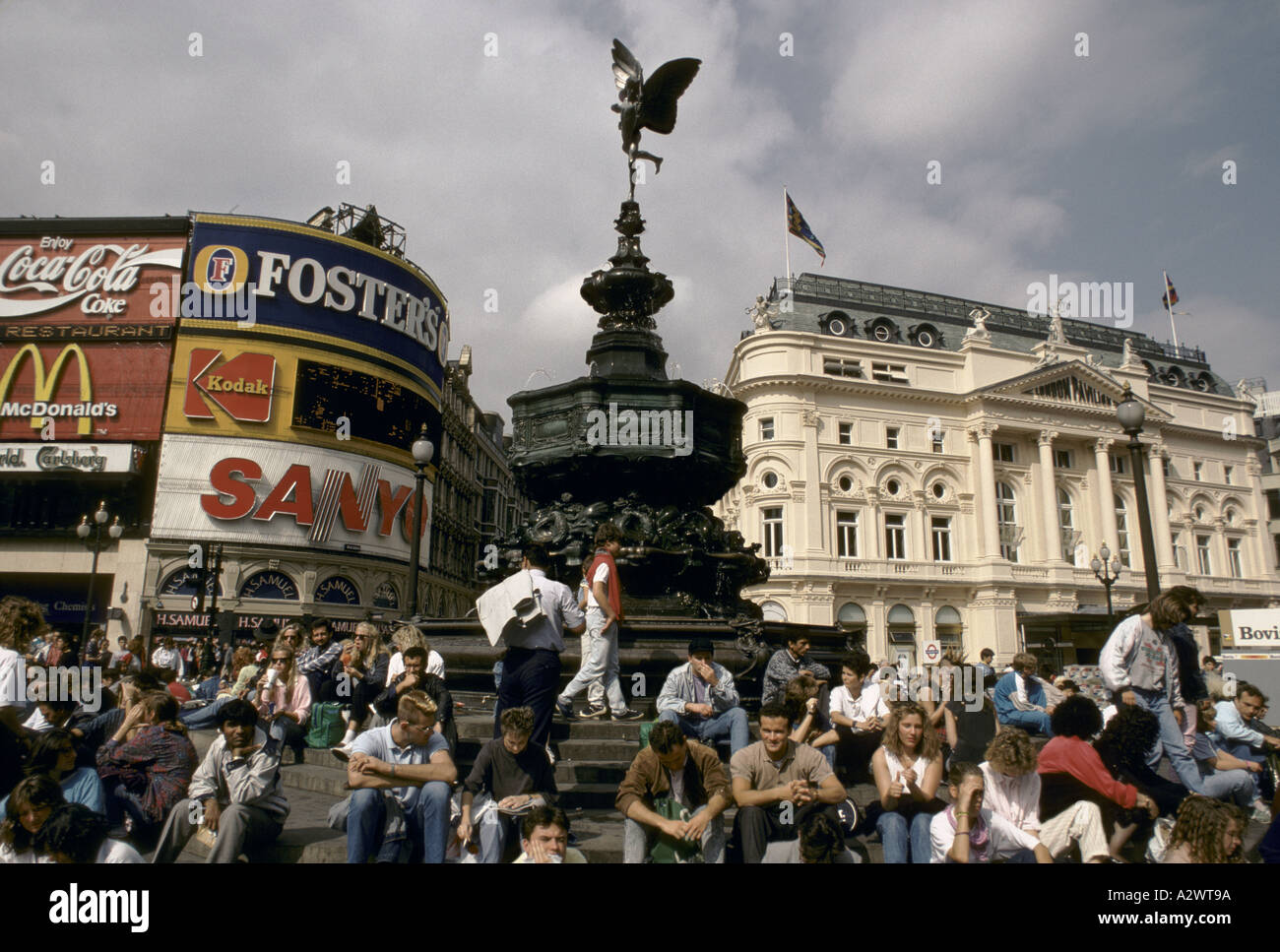 tourists sitting under the statue of eros in piccadilly circus, london Stock Photo