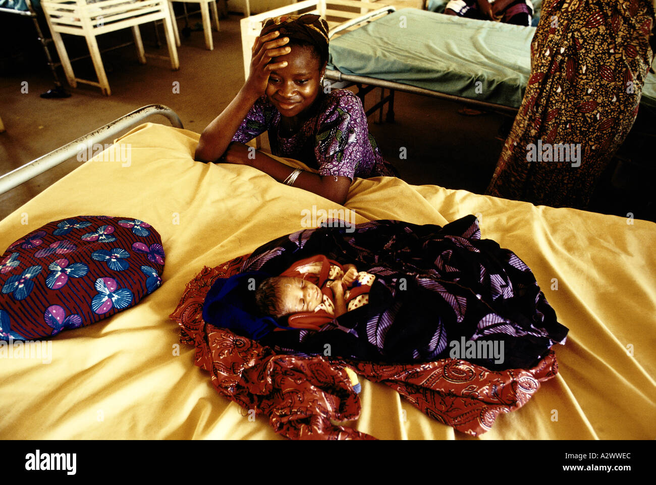 A baby lies on the bed while the proud mother  looks on in the post natal ward at Segbwema Hospital, Sierra Leone, Africa Stock Photo