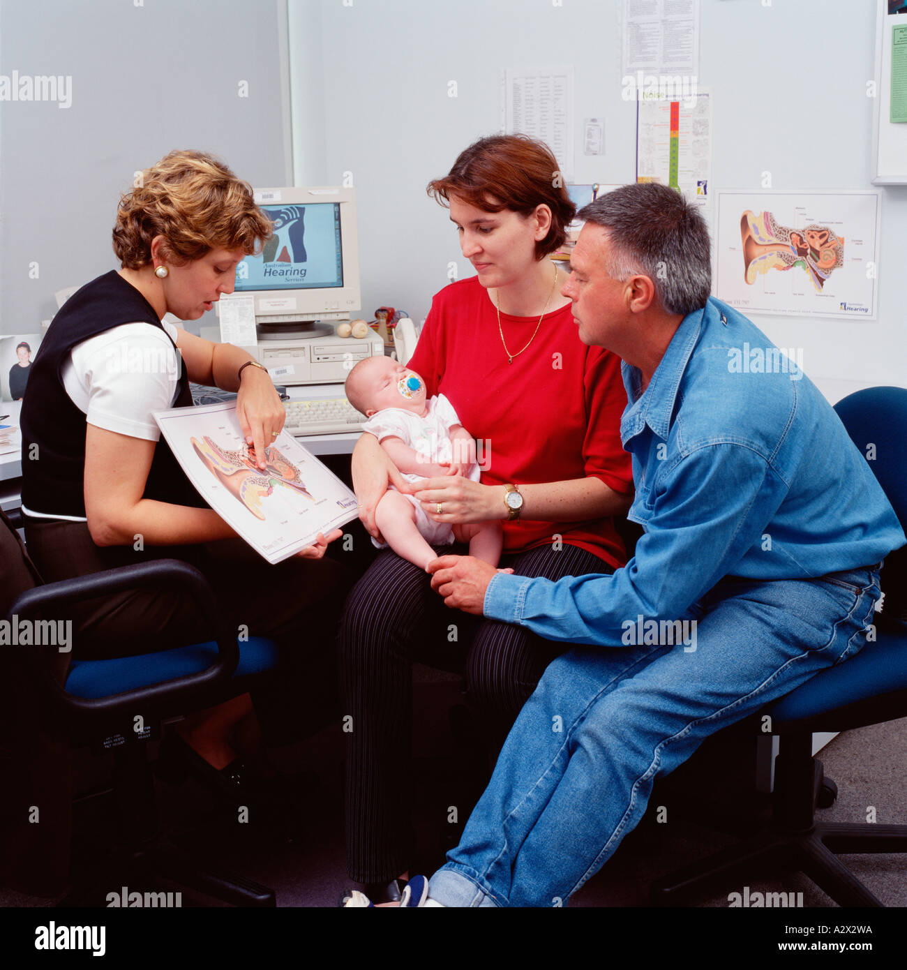 Couple with new baby in hospital consulting room for hearing test with woman doctor. Stock Photo