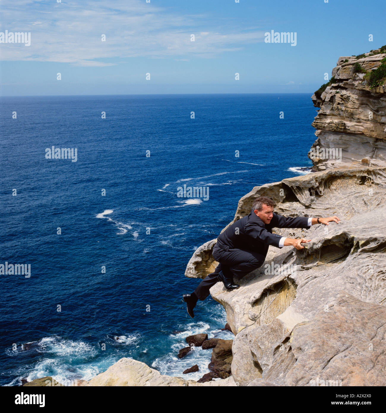 Concept. Business man in suit climbing a cliff with view of the ocean horizon. Stock Photo