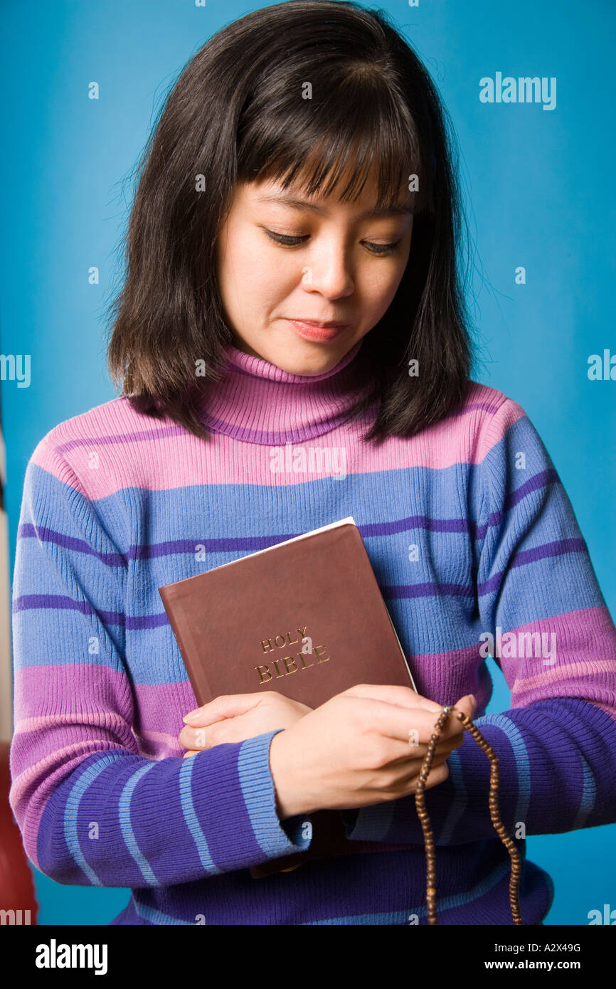 Young Asian woman holding a bible to her chest and rosary beads in her hand. Stock Photo