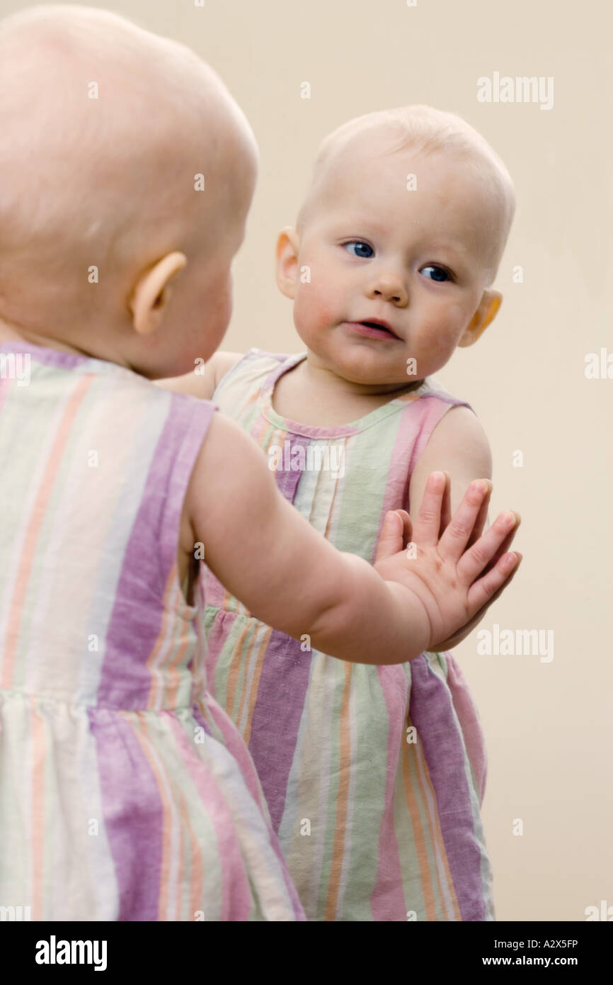 Eight 8 month old baby girl recognizes herself as she looks into a mirror. Stock Photo