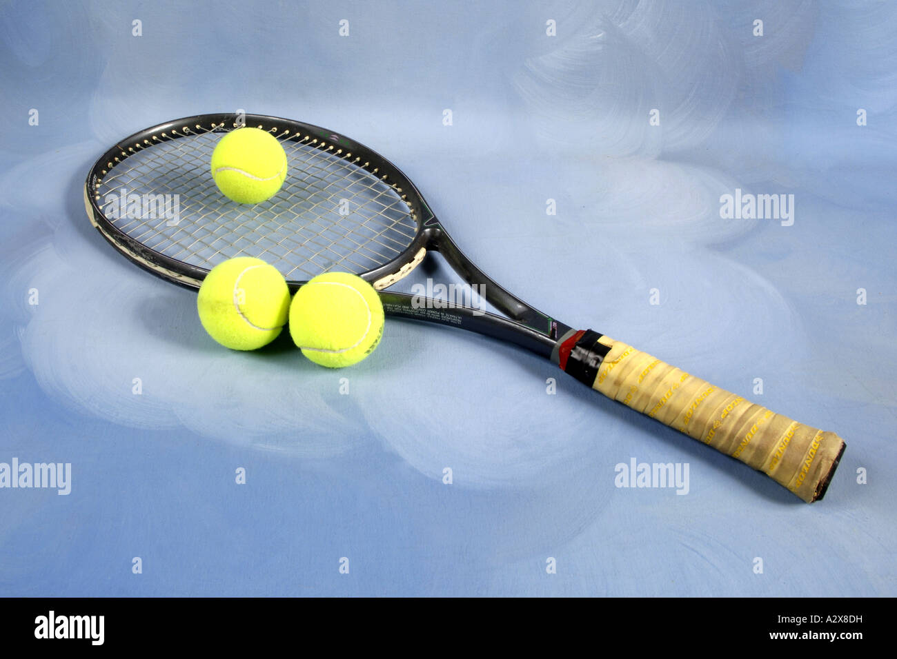 Tennis racket and three yellow balls against a blue background Stock Photo