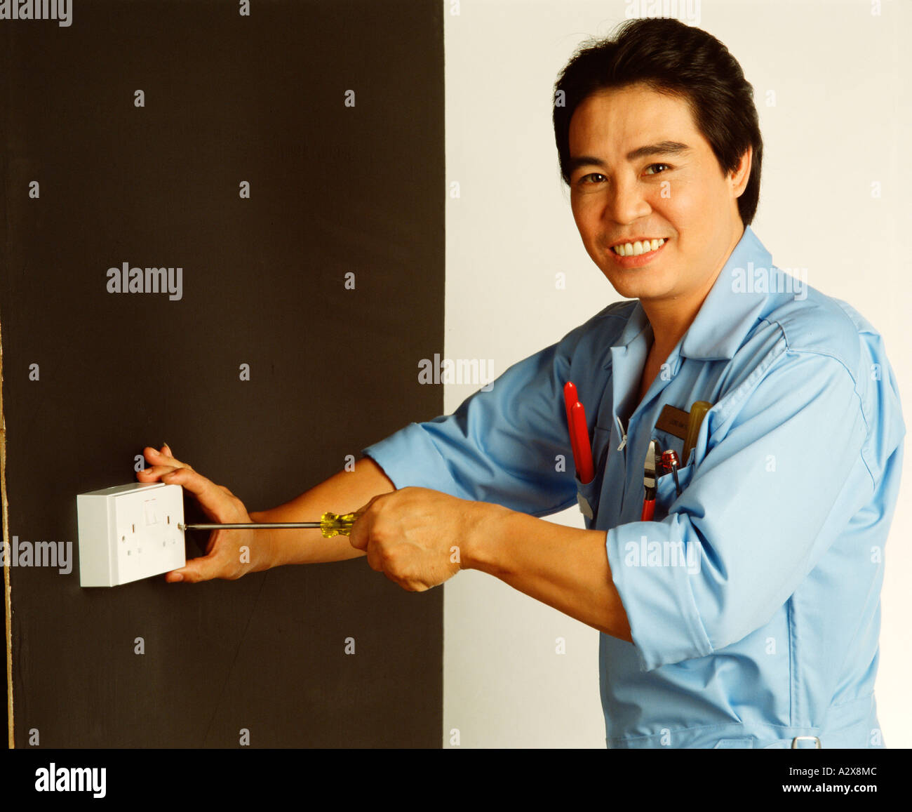 Chinese tradesman electrician demonstrating fitting electrical socket high wall placement. Stock Photo