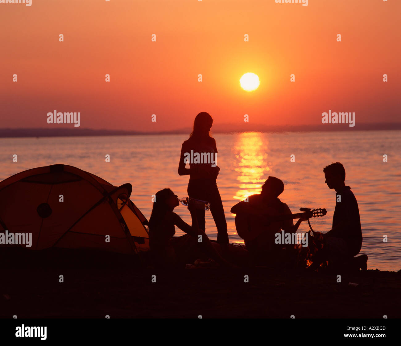 Group of young people camping on a beach at sunset. Stock Photo