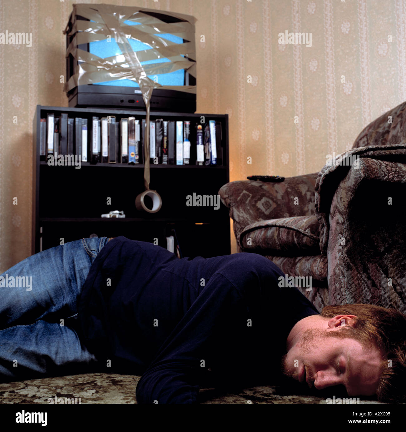 man lying on floor in front of tv wrapped up colour indoors Stock Photo
