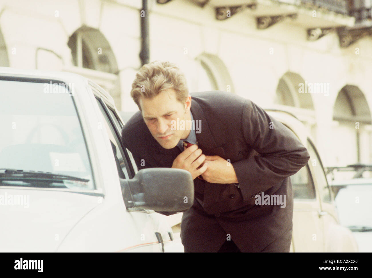 Businessman in city street adjusting his tie with aid of car mirror. Stock Photo